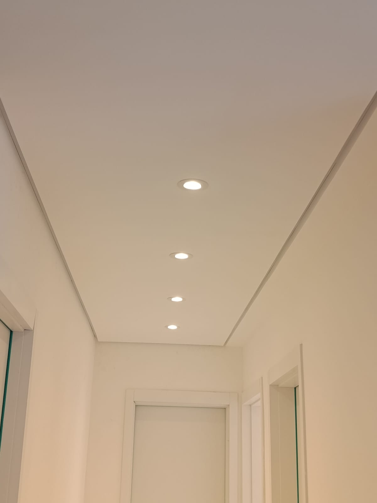 corredor branco com sancas de gesso e spots de LED embutidos no teto, portas brancas ao fundo  — texto:  